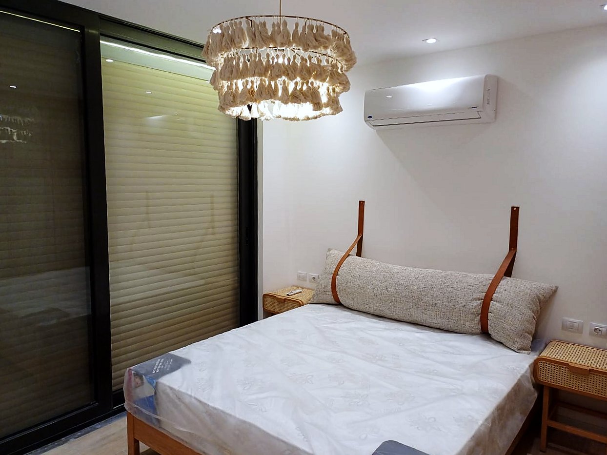 Timber bed with a bolster hung on leather straps, rattan bedside tables and a tassel chandelier