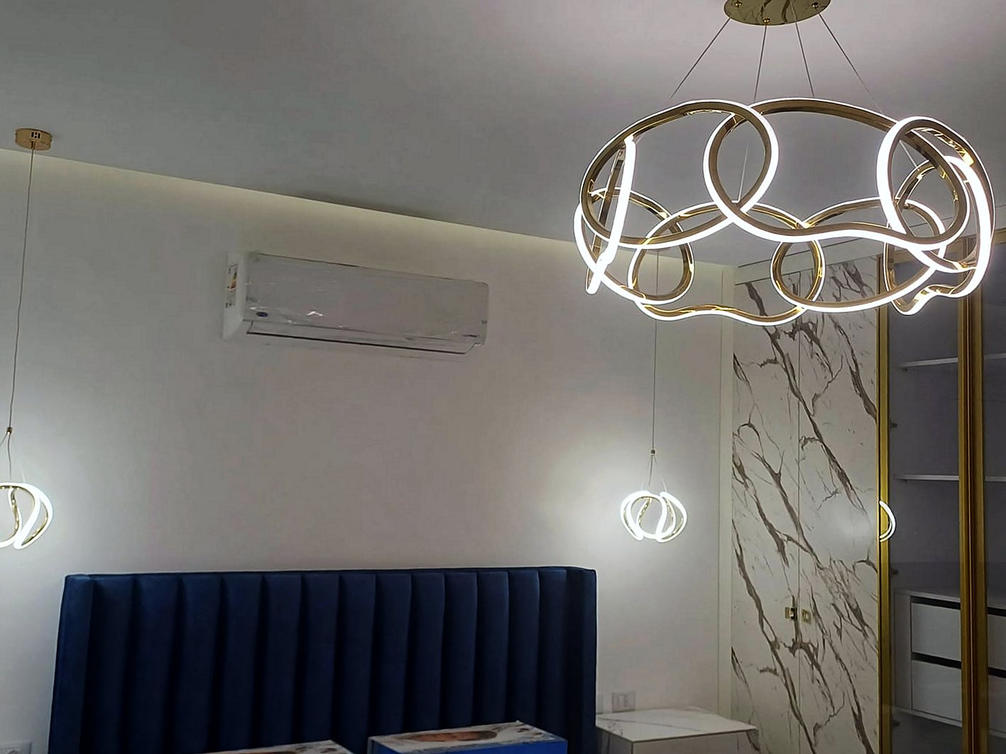 Navy velvet channel headboard under a cove-lit ceiling with ring pendant