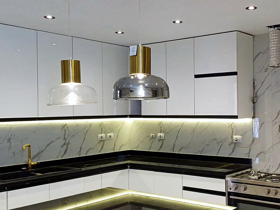 White gloss kitchen with brass pendants, LED-lit black island and marble-look splashback in a North Coast villa
