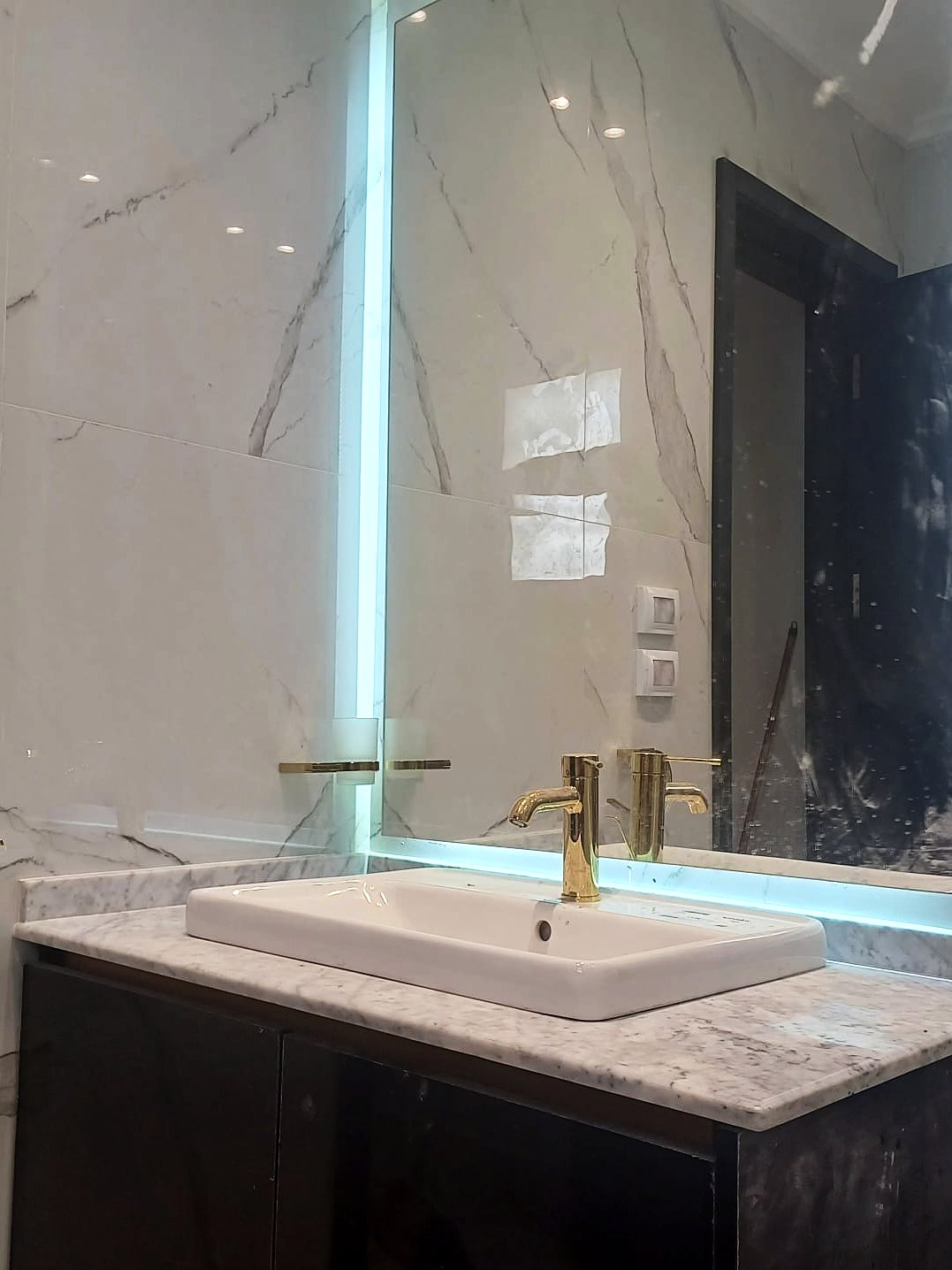 Backlit mirror over a marble vanity with a brass tap