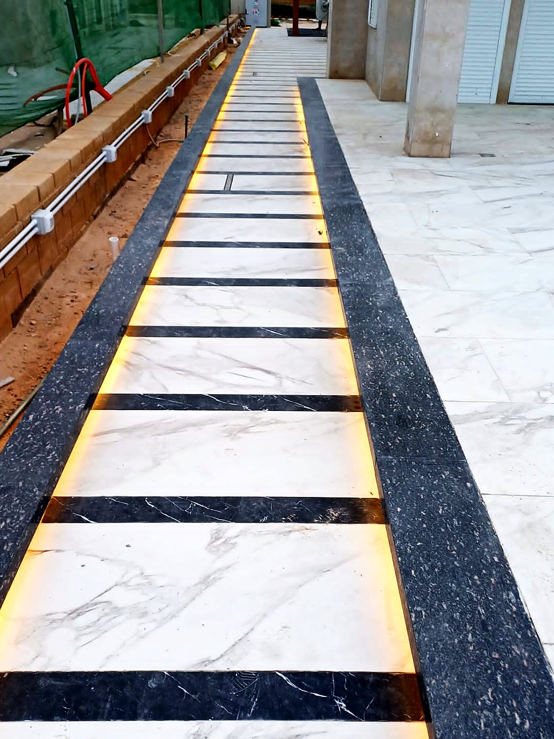 White marble walkway with dark granite bands and LED strips being laid