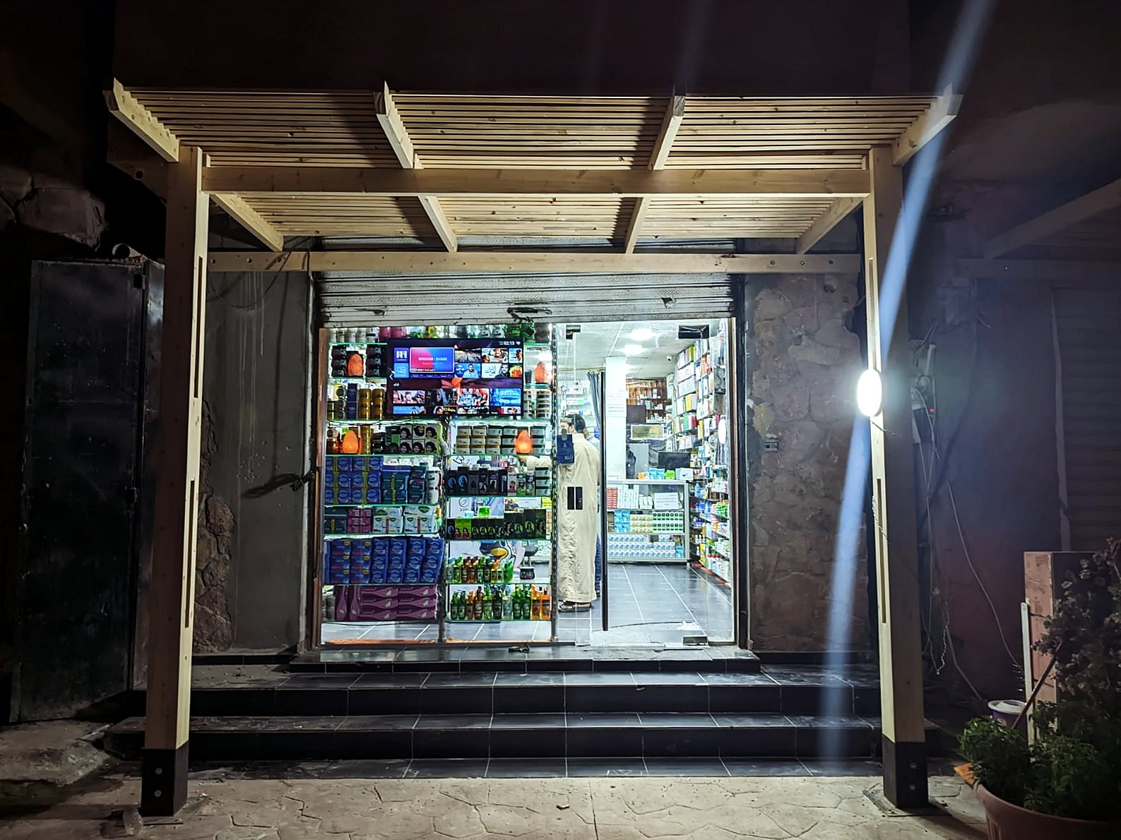 Timber pergola over a lit pharmacy entrance at night in Siwa