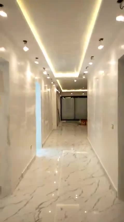 Finished corridor leading to a living area, with a cove-lit ceiling and marble-look floor — on site