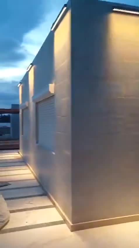 Finished villa exterior at dusk with wall lights, roller shutters and banded paving — on site