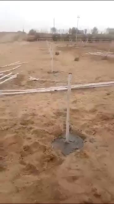 White fence posts set in concrete across a sand yard, rails laid out beside them — on site
